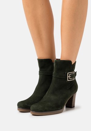 Bottes chelsea en daim vert foncé avec un bout arrondi, un petit talon et une boucle sur le côté pour un détail élégant. Texture lisse et design à la mode.