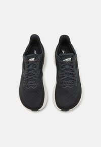 Baskets de sport noires avec une tige texturée, accents gris et lacets à motifs. La semelle a une forme courbe avec une couleur plus claire en contraste.