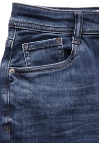 Jeans de mezclilla azul oscuro que presentan un primer plano de la cinturilla, el bolsillo delantero y detalles de costura en contraste. Textura suave con costuras definidas.