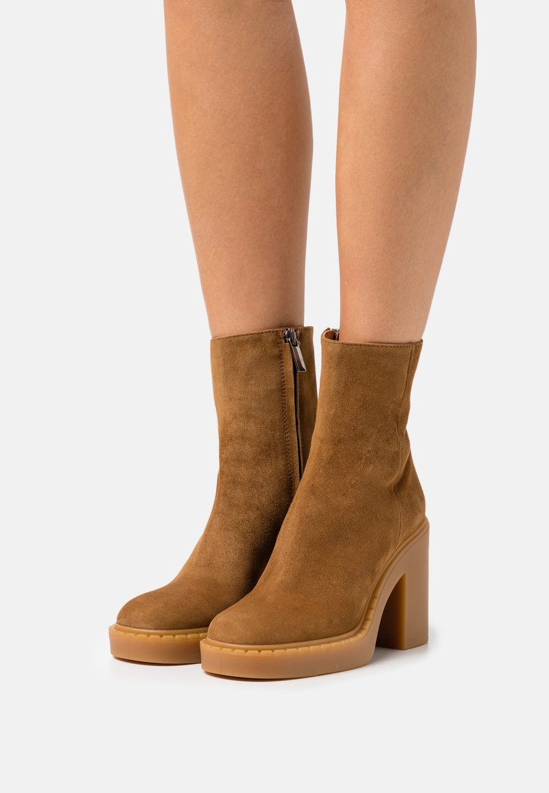 Brown suede ankle boots with a round toe, side zipper, and a chunky heel. Features a textured design and a rubber sole.