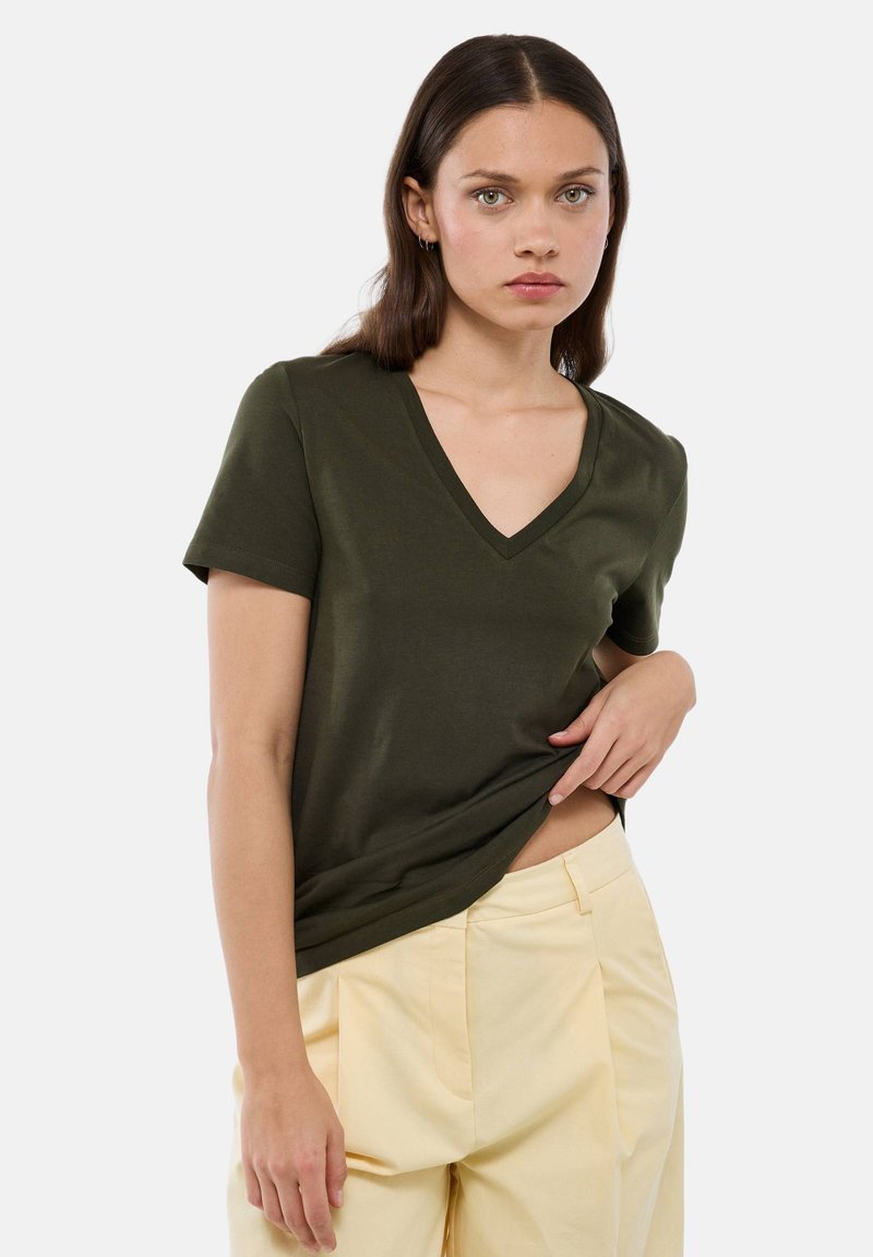 T-shirt vert olive à col en V, manches courtes, en tissu doux. Associe à un pantalon taille haute jaune clair, offrant une coupe décontractée.