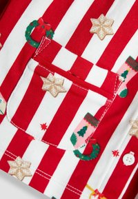 Sarkans un balts svītrots audums ar dažādiem svētku motīviem, tostarp vainagiem, sniegpārsliņām un zeķēm. Satur kabatu.