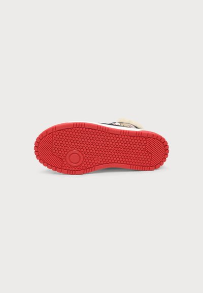 Chaussure à semelle en caoutchouc avec un dessin rouge à petits cercles et un motif circulaire près du talon, sur un fond clair uni.