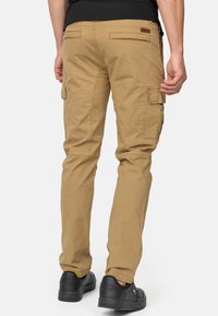 Spodnie cargo w khaki, z wieloma bocznymi kieszeniami, luźnym krojem i widocznymi szwami. Noszone z czarnymi trampkami.