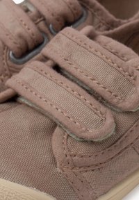 Pantofi din pânză de culoare maro deschis, cu două benzi Velcro. Prezintă un material texturat, vârf rotund și cusături contrastante pe partea superioară.
