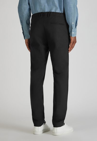 Zwarte broek met een ontspannen pasvorm, elastische tailleband en twee achterzakken. Gepaard met witte sneakers en een blauwe overhemd met knopen.