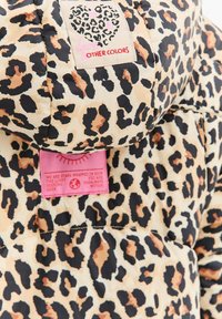 Pufová bunda s leopardím potiskem, která má béžový podklad s černými a hnědými skvrnami. Obsahuje růžové vnitřní štítky s textem a dekorativním prošitím.