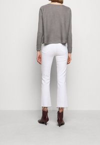 Pull gris côtelé avec une coupe courte. Associé à un jean blanc évasé avec des bords effilochés. Bottines marron à talon petit.