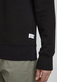 Zwarte sweatshirt met ribgebreide mouwen en zoom. Heeft een klein logo-label aan de zijkant. Gemaakt van een zachte katoenmix.