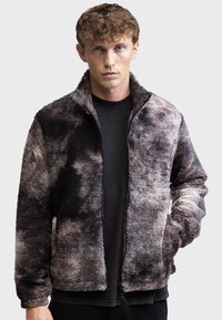 Strukturierte Fleecejacke mit durchgehendem Reißverschluss, hohem Kragen und einer Kombination aus grauen und schwarzen abstrakten Mustern. Geeignet für die Freizeit.