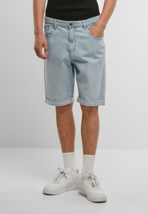 Light blue denim shorts with rolled cuffs, featuring a classic five-pocket design and a button closure. Worn with white sneakers and socks.