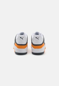 Sneakerit, joissa on pääasiassa valkoinen yläosa, harmaat yksityiskohdat ja kirkas oranssi koristelu. Niissä on tekstuurilla varustettu kantapää ja kestävä kumipohja.