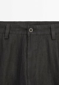 Tummanharmaat pellavahousut, joissa on nappisuljenta ja vyölenkit, sileä pinta ja hentoa ompelua.