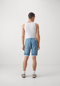 Shorts en denim bleu clair avec ourlets retroussés, dotés de poches arrière et d'une patch en cuir à la taille. Associés à un débardeur blanc et à des chaussettes.