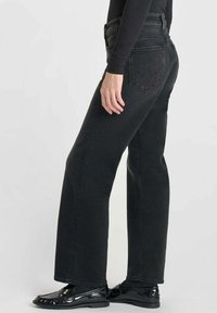 Zwarte denim jeans met een recht naar beneden gesneden ontwerp, vijf zakken en subtiele stiksels op de achterzak. Gecombineerd met zwart, glanzend schoeisel.