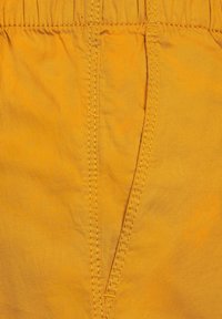 Gult bomullstyg med en synlig sydd söm och en trekantig kil, med en mjuk yta och elastisk midjeresår.