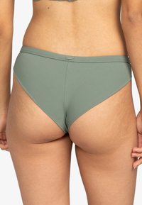 Olivgrön bikiniunderdel med ribbad textur, med låg midja och diskret logotag på midjebandet.