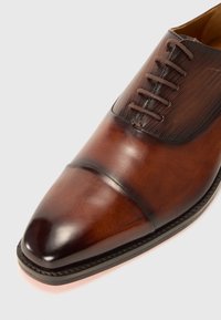 Zapato de vestir de cuero marrón con punta afilada, superficie suave, tejido texturizado en la parte superior y cordones marrones.