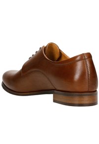Braune Lederdressschuhe mit glatter Oberfläche, runder Zehenpartie, sechs Ösen für Schnürsenkel und einem gestapelten Holzabsatz. Das Innenfutter ist beige.