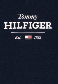 Granatowa bawełniana koszulka z białym napisem "Tommy HILFIGER" oraz rokiem założenia 1985, a także prostokątnym logo w czerwonym, białym i niebieskim kolorze.
