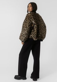Jakna od lažne krznene tkanine s uzorkom leoparda, slobodnog kroja, zaobljenim ramenima i rebrastim manžetama, uparena s crnim širokim hlačama i čvrstim čizmama.