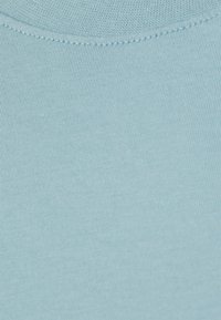 Ljusblått bomullstyg med en slät textur. Närbilden framhäver de fina ribbade detaljerna och de rena sömmarna längs kanten.