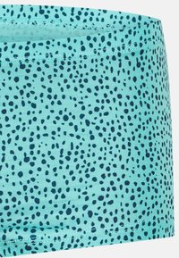 Tessuto di colore turchese con motivi e macchie blu scuro, caratterizzato da una superficie rigata e un orlo cucito. Adatto per costumi da bagno o abbigliamento sportivo.