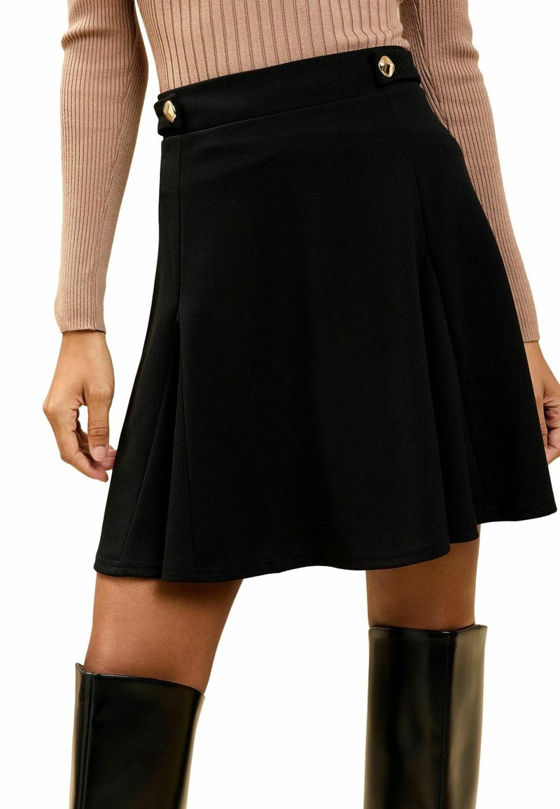 Black flared skirt with a smooth texture, featuring gold-tone buttons on the waistband and a knee-length design, paired with knee-high black boots.