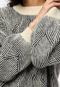 Strickpullover mit einem geometrischen schwarz-weißen Streifenmuster, einem weichen cremefarbenen Rundhalsausschnitt und strukturierten Ärmeln.