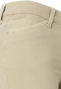 Los pantalones de mezclilla beige presentan una textura suave, corte recto y bolsillos traseros con costuras sutiles. Herrajes ocultos en la cintura.