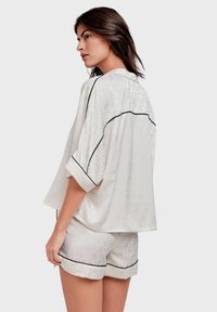 Pyjama en satin blanc avec un motif texturé, des finitions noires et une coupe décontractée. Le haut possède des manches courtes et un design ample.