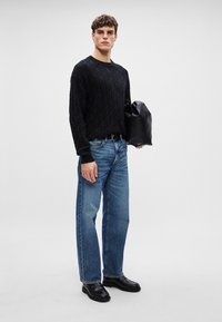 Camicia a maniche lunghe nera a motivo, jeans dritti blu chiaro e scarpe di pelle nere. Tiene una borsa nera. Design semplice e casual.