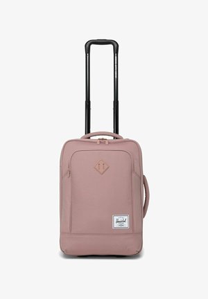 Valise à roulettes douce et portable de couleur rose pastel avec une poignée télescopique noire prolongée et une poche zippée à l'avant, étiquette Herschel visible.