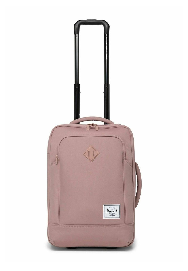 Valise à roulettes douce et portable de couleur rose pastel avec une poignée télescopique noire prolongée et une poche zippée à l'avant, étiquette Herschel visible.