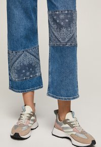 Blå denimcroppade byxor med mönstrade paneler och råa sömmar, kombinerat med beige, rosa och grå sneakers med vita accenter och en strukturerad sula.