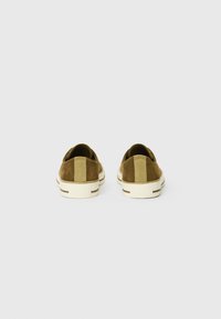 Zapatillas de ante marrón con una franja beige en contraste en el talón, suela de goma blanca y detalle texturizado en la parte superior. Vista trasera mostrada.
