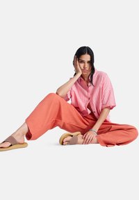 Ριγέ κόκκινο και λευκό πουκάμισο με κοντά μανίκια και κουμπιά, κοραλλί παντελόνι με φαρδιά πόδια και καφέ σανδάλια με μαξιλαρωμένη σόλα.