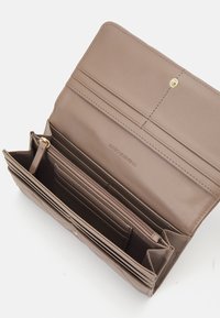 Καφέ συνθετικό πορτοφόλι με πολλαπλές θήκες καρτών, με τσέπη που κλείνει με φερμουάρ και χρυσό κλείσιμο με κουμπί. Λείο υλικό με μινιμαλιστικό σχέδιο.