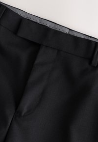 Pantaloni neri su misura con una texture liscia, dotati di una fascia in vita piatta e una sottile fodera a spina di pesce all'interno.