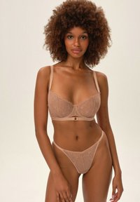 Biustonosz i stringi w kolorze cielistym, wykonane z koronkowego materiału z florystycznymi wzorami, z regulowanymi ramiączkami oraz centralnym akcentem w postaci ozdobnego elementu na biustonoszu.