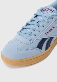 Jasnoniebieskie zamszowe sneakersy z granatowymi akcentami, płaskimi sznurówkami i gumową podeszwą. Zawierają logo marki na języku i boku.