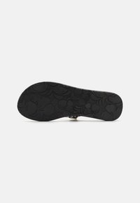 Black rubber sandal sole with floral pattern, featuring detailed texture and raised accents for grip. Roxy branding is visible in the design.