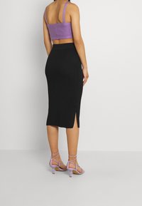 Lila gerippter Croptop, schwarze gerippte Midirock mit seitlichem Schlitz und lavendelfarbene, geflochtene, hochhackige Sandalen mit Blockabsatz.
