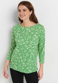 Grünes Langarmoberteil mit floralem Muster und weißen Blumen, Rundhalsausschnitt und einem leicht abgerundeten Saum. Das Material wirkt leicht.