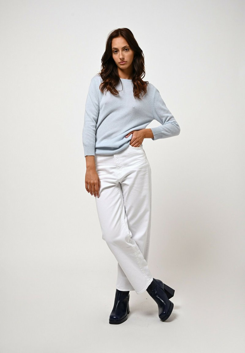 Maglione a maglia azzurro chiaro con scollatura rotonda, abbinato a pantaloni bianchi a gamba dritta. Stivali neri con tacco completano l'outfit.