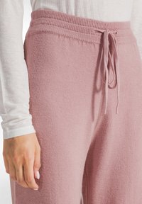 Helle rosa, weiche Strick-Jogger mit einem gerippten Bund. Verfügt über einen Kordelzug und eine strukturierte Oberfläche, kombiniert mit einem weißen Langarmtop.