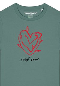 Groene katoenen T-shirt met een rode hartdruk met verstrengelde armen, accentueert door bladeren en de tekst "zelfliefde" in zwarte script.
