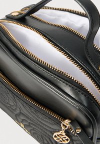 Czarna, teksturowana skórzana torebka z złotymi zamkami błyskawicznymi i okuciami; posiada wiele komór zapinanych na zamek oraz gładkie, materiałowe wnętrze.