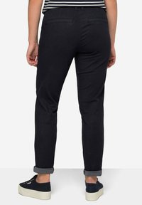 Pantaloni in denim neri con taglio dritto e orli risvoltati, dotati di due tasche posteriori e una texture liscia. Indossati con sneaker scure.