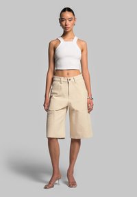 Top corto bianco a coste con spalline larghe, abbinato a pantaloni di jeans beige a metà coscia con tasche frontali e chiusura con bottone.